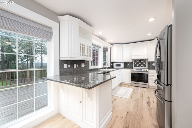 kitchen featuring white cabinets, a peninsula, stainless steel appliances, and light wood-style flooring