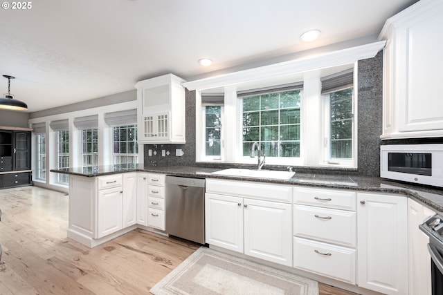 kitchen with light wood finished floors, a peninsula, a sink, white cabinets, and appliances with stainless steel finishes