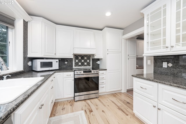 kitchen with white microwave, stainless steel electric stove, light wood-style flooring, white cabinetry, and a sink