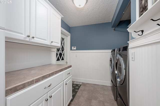 laundry area with a wainscoted wall, washer and dryer, a textured ceiling, cabinet space, and light tile patterned flooring