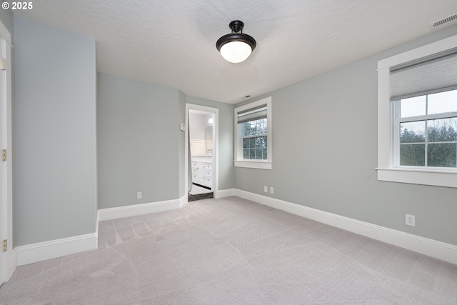 unfurnished bedroom with visible vents, a textured ceiling, ensuite bath, carpet flooring, and baseboards