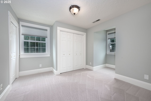 unfurnished bedroom with visible vents, a textured ceiling, a closet, carpet flooring, and baseboards