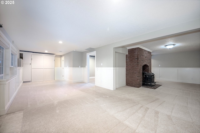 unfurnished living room featuring recessed lighting, light colored carpet, wainscoting, and a wood stove