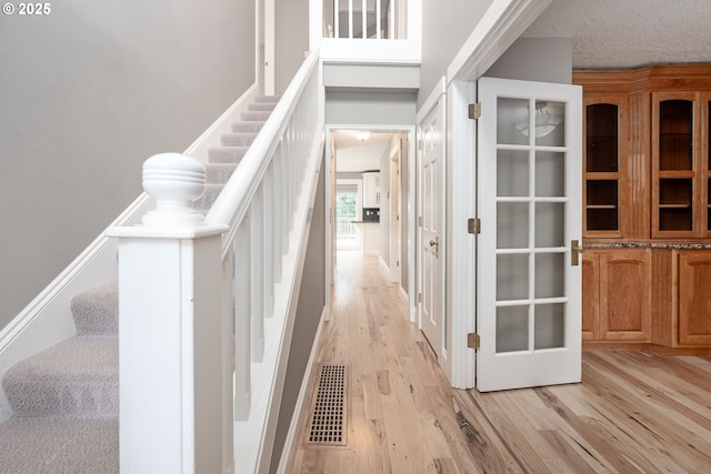 hallway with stairway, visible vents, light wood finished floors, and a textured ceiling