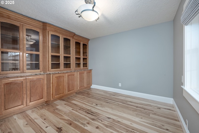 interior space featuring light wood finished floors, a textured ceiling, and baseboards