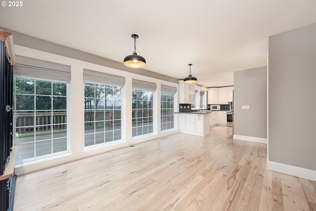 unfurnished living room with a textured ceiling, baseboards, light wood finished floors, and a sink