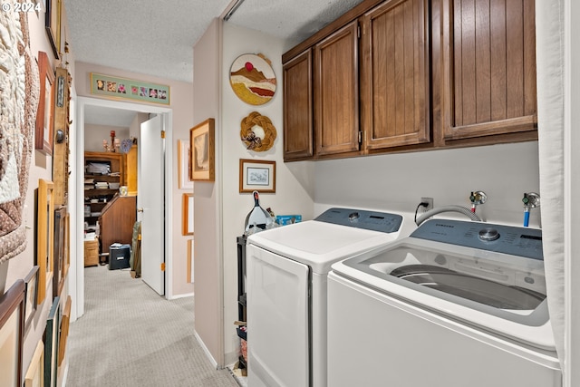 clothes washing area with cabinets, a textured ceiling, washing machine and clothes dryer, and light carpet