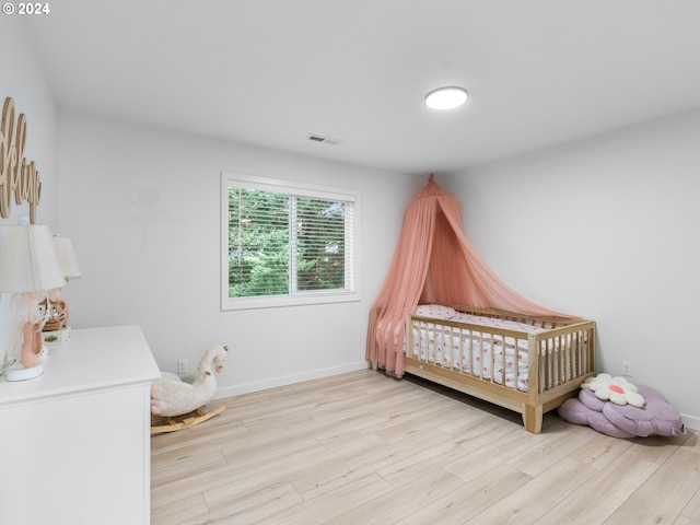 bedroom featuring light wood-type flooring and a crib