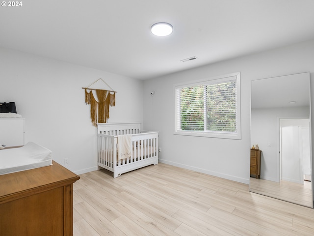 bedroom with light wood-type flooring and a nursery area