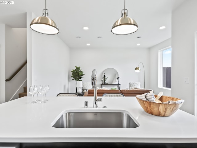 kitchen with light countertops, hanging light fixtures, open floor plan, a kitchen island with sink, and a sink