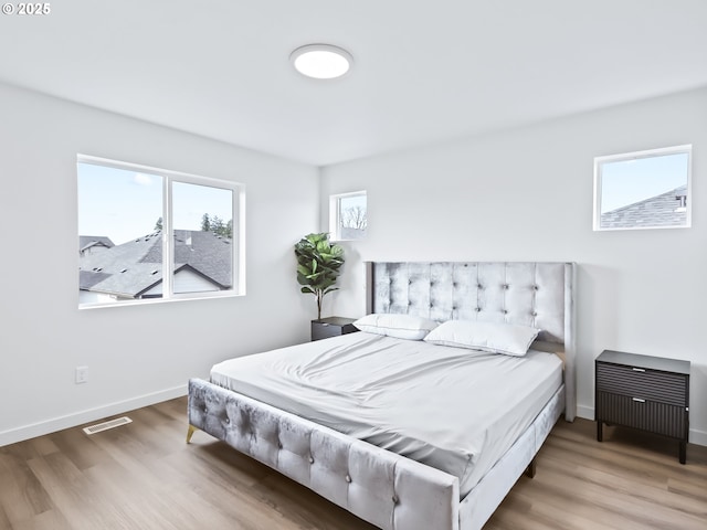 bedroom with baseboards, visible vents, and wood finished floors