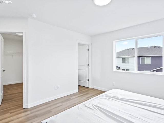 bedroom featuring a walk in closet, a closet, light wood-style flooring, and baseboards