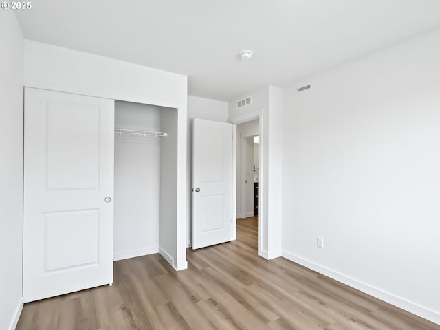 unfurnished bedroom with light wood-style flooring, a closet, visible vents, and baseboards