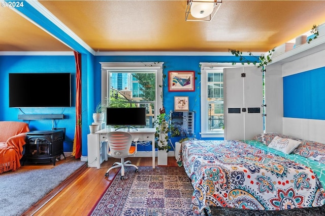 bedroom featuring a textured ceiling, a wood stove, crown molding, and wood-type flooring