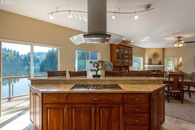 kitchen with light stone countertops, island range hood, track lighting, stainless steel gas cooktop, and light tile floors