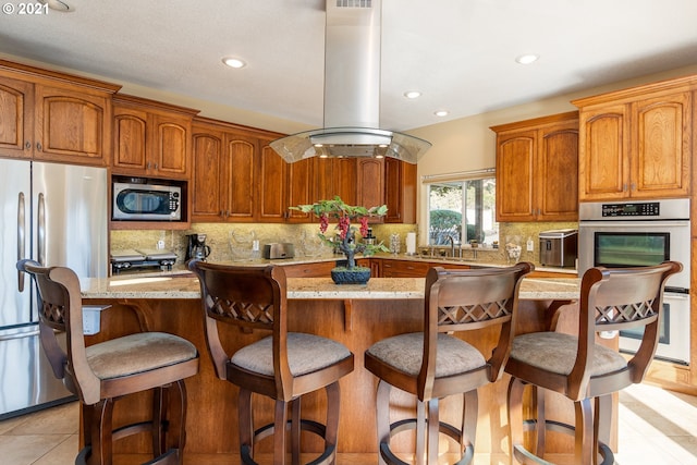 kitchen with appliances with stainless steel finishes, backsplash, a kitchen breakfast bar, island exhaust hood, and light tile floors