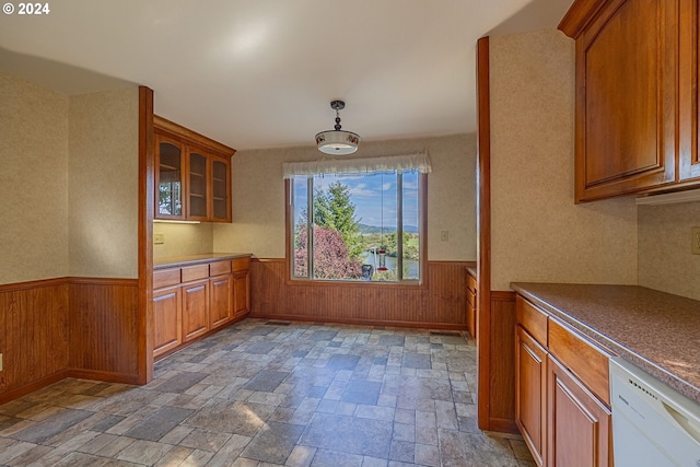 91235 N Bank Ln, Coquille, OR 97423 - kitchen with glass insert cabinets, a wainscoted wall, white dishwasher, brown cabinetry, and stone finish floor