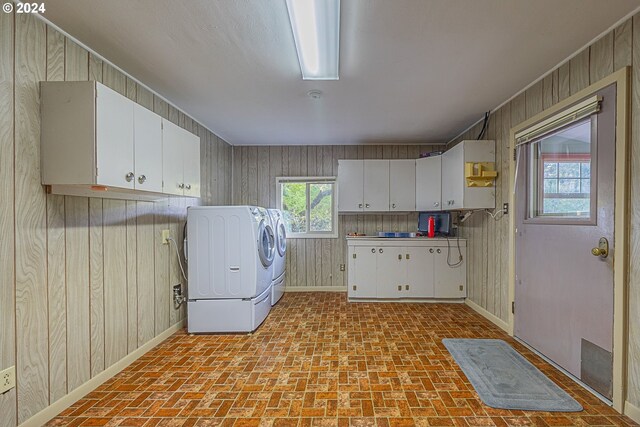 laundry area featuring washing machine and dryer, wood walls, and cabinets