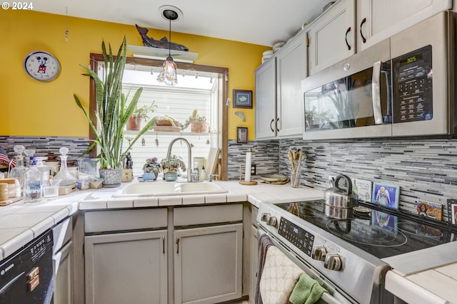 kitchen with tile counters, pendant lighting, sink, and appliances with stainless steel finishes