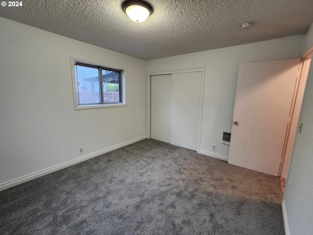 unfurnished bedroom featuring a textured ceiling, heating unit, dark colored carpet, and a closet