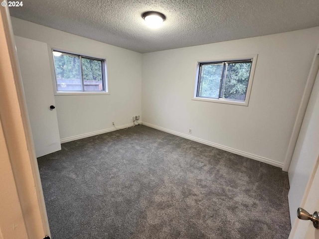 spare room featuring dark colored carpet and a textured ceiling