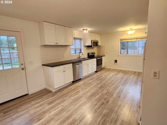 kitchen with tasteful backsplash, stainless steel appliances, sink, white cabinets, and light hardwood / wood-style floors