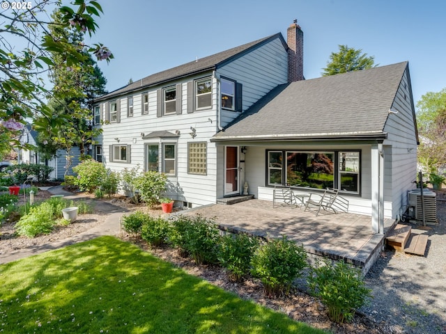 back of property with a lawn, roof with shingles, central AC, and a chimney