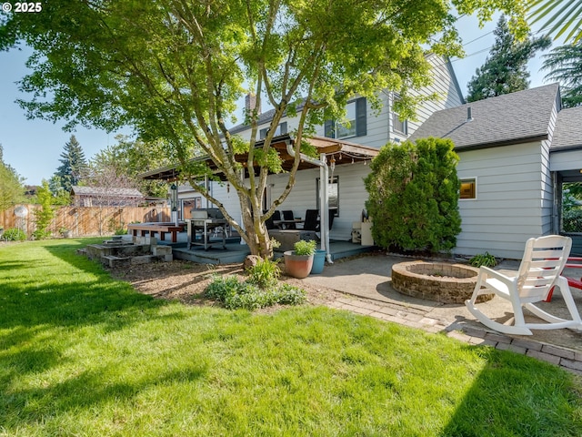 back of property featuring fence, a patio, a shingled roof, an outdoor fire pit, and a yard