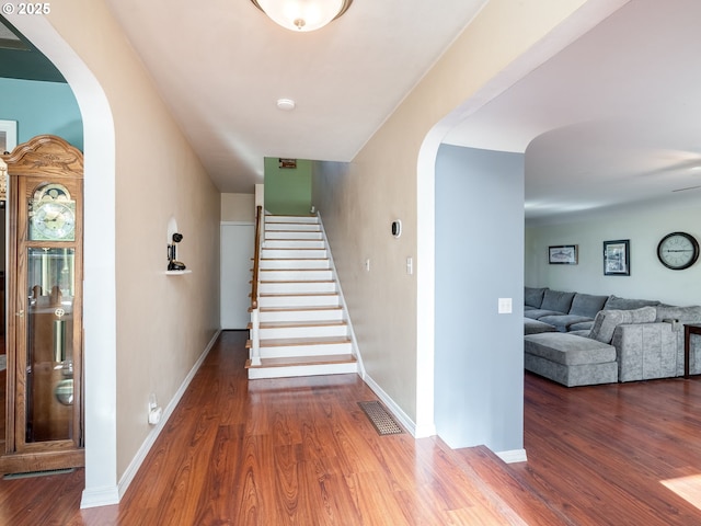 staircase featuring visible vents, arched walkways, baseboards, and wood finished floors