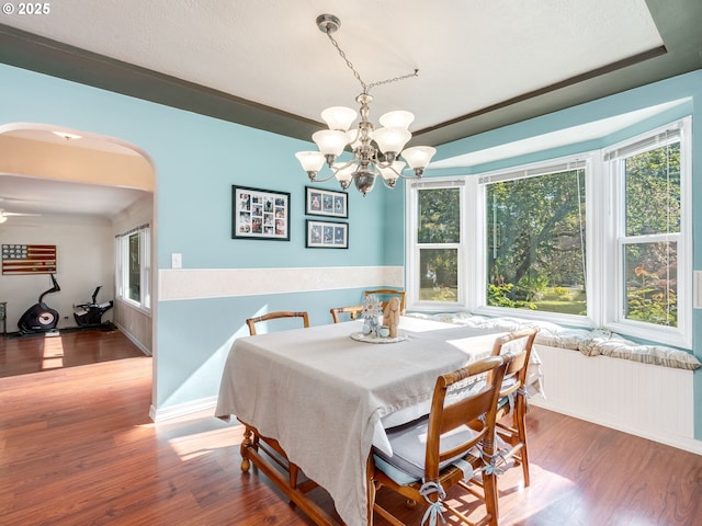 dining room with arched walkways, wood finished floors, a chandelier, and a wealth of natural light