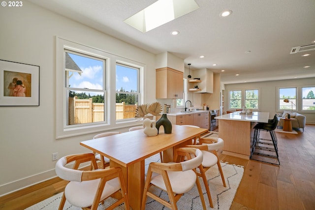 dining room featuring sink, light hardwood / wood-style floors, and a skylight