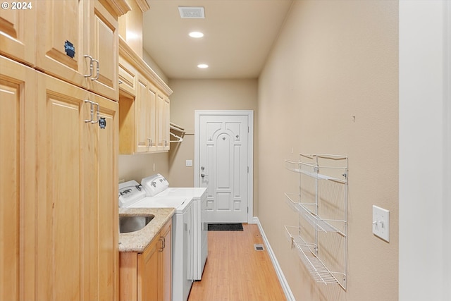 laundry room with sink, independent washer and dryer, light wood-type flooring, and cabinets