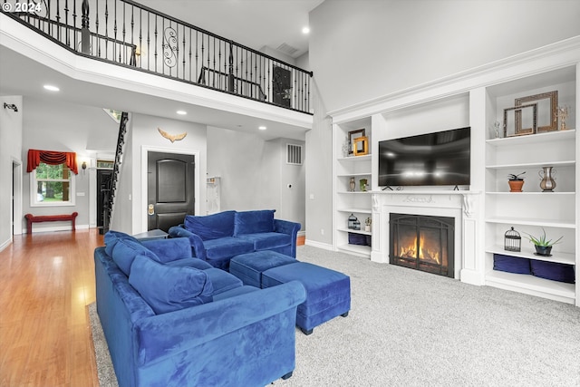 living room with built in features, wood-type flooring, and a high ceiling