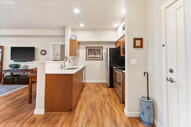 kitchen featuring sink, stainless steel appliances, light wood-type flooring, and kitchen peninsula