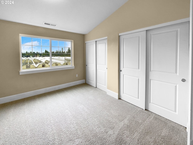 unfurnished bedroom with lofted ceiling, light colored carpet, and multiple closets