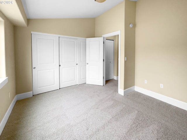 unfurnished bedroom with lofted ceiling, a closet, and light carpet