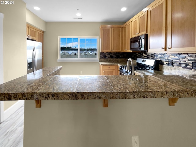 kitchen featuring light wood-type flooring, stainless steel appliances, kitchen peninsula, a kitchen bar, and decorative backsplash