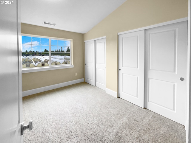 unfurnished bedroom with multiple closets, lofted ceiling, and light colored carpet