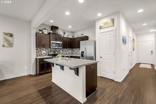 kitchen featuring appliances with stainless steel finishes, dark brown cabinets, an island with sink, a breakfast bar, and dark wood-type flooring