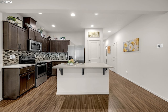 kitchen featuring hardwood / wood-style flooring, a kitchen bar, a kitchen island with sink, and appliances with stainless steel finishes