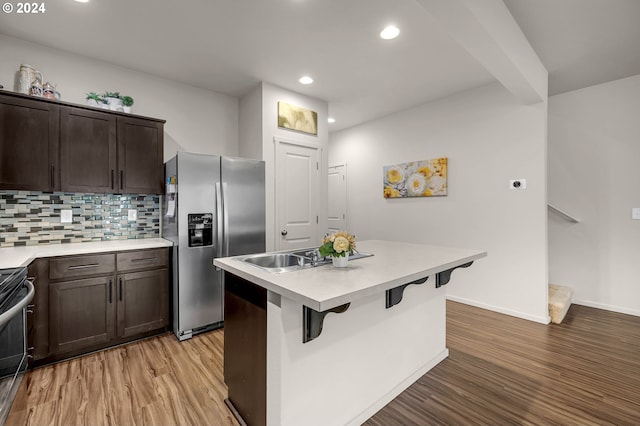 kitchen featuring stainless steel fridge, light wood-type flooring, decorative backsplash, a kitchen breakfast bar, and black range oven