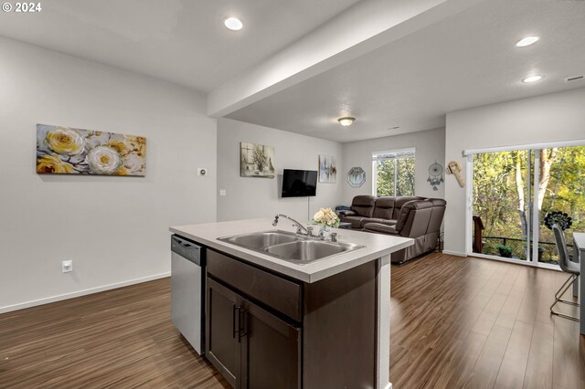 kitchen with dark hardwood / wood-style flooring, a center island with sink, sink, stainless steel dishwasher, and dark brown cabinets