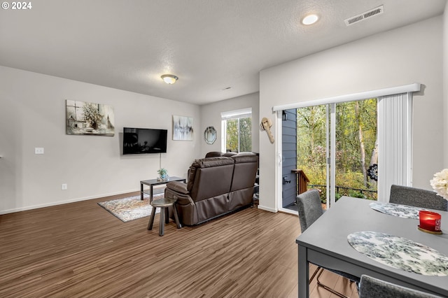 living room with baseboards, a textured ceiling, visible vents, and wood finished floors