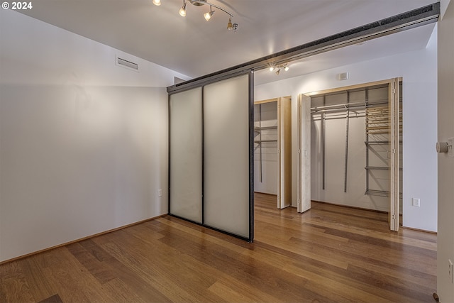 unfurnished bedroom featuring hardwood / wood-style floors, two closets, and rail lighting