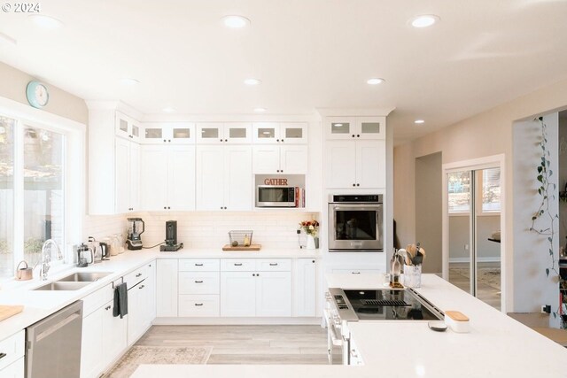 kitchen featuring white cabinetry, stainless steel appliances, light hardwood / wood-style floors, sink, and backsplash