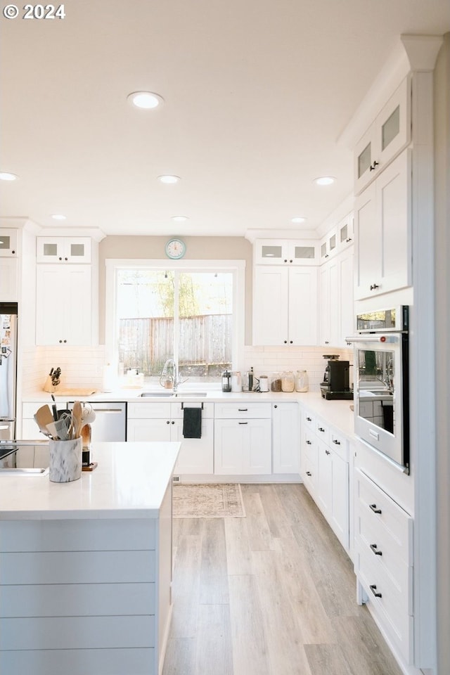 kitchen with backsplash, white cabinetry, and stainless steel oven