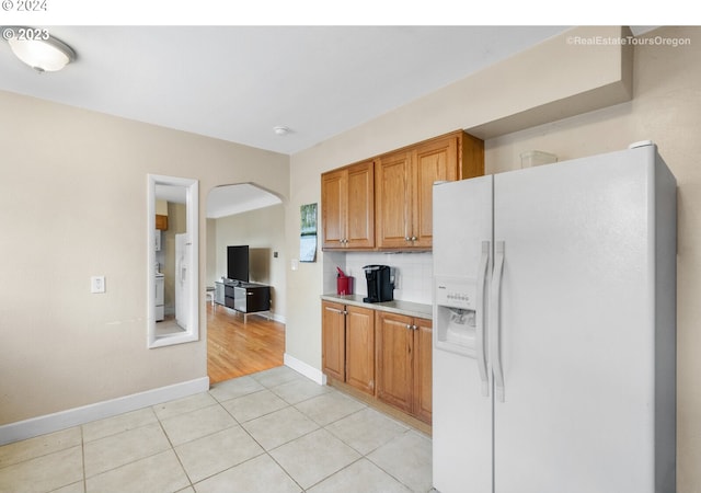 kitchen featuring washer / clothes dryer, decorative backsplash, light tile patterned flooring, and white refrigerator with ice dispenser