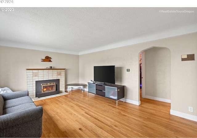 living room featuring a tile fireplace, a textured ceiling, and light wood-type flooring