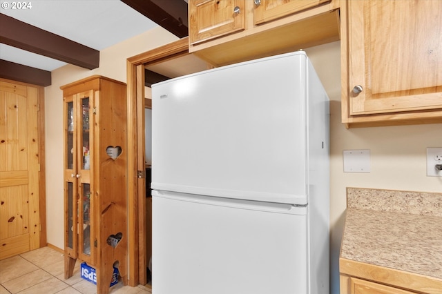 kitchen with light tile patterned floors, beam ceiling, light brown cabinets, and white fridge