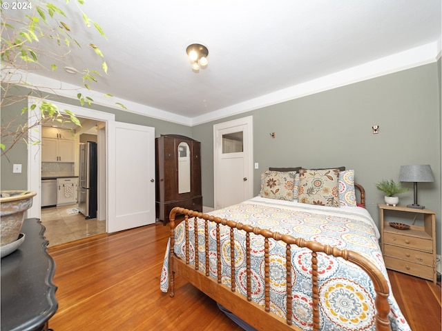 bedroom with stainless steel fridge, light wood-type flooring, and ensuite bath